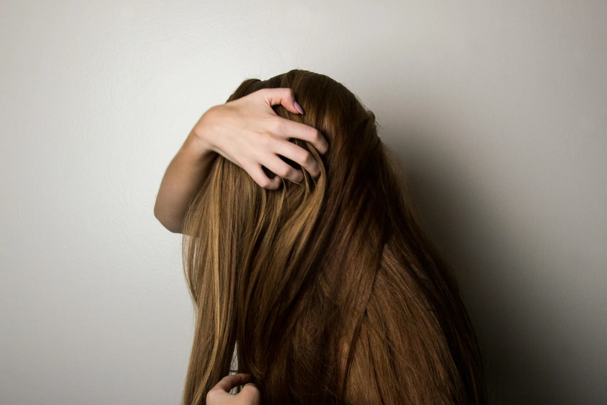 A woman with flowing hair gently touching her head, prevent hair loss by doing scalp treatment