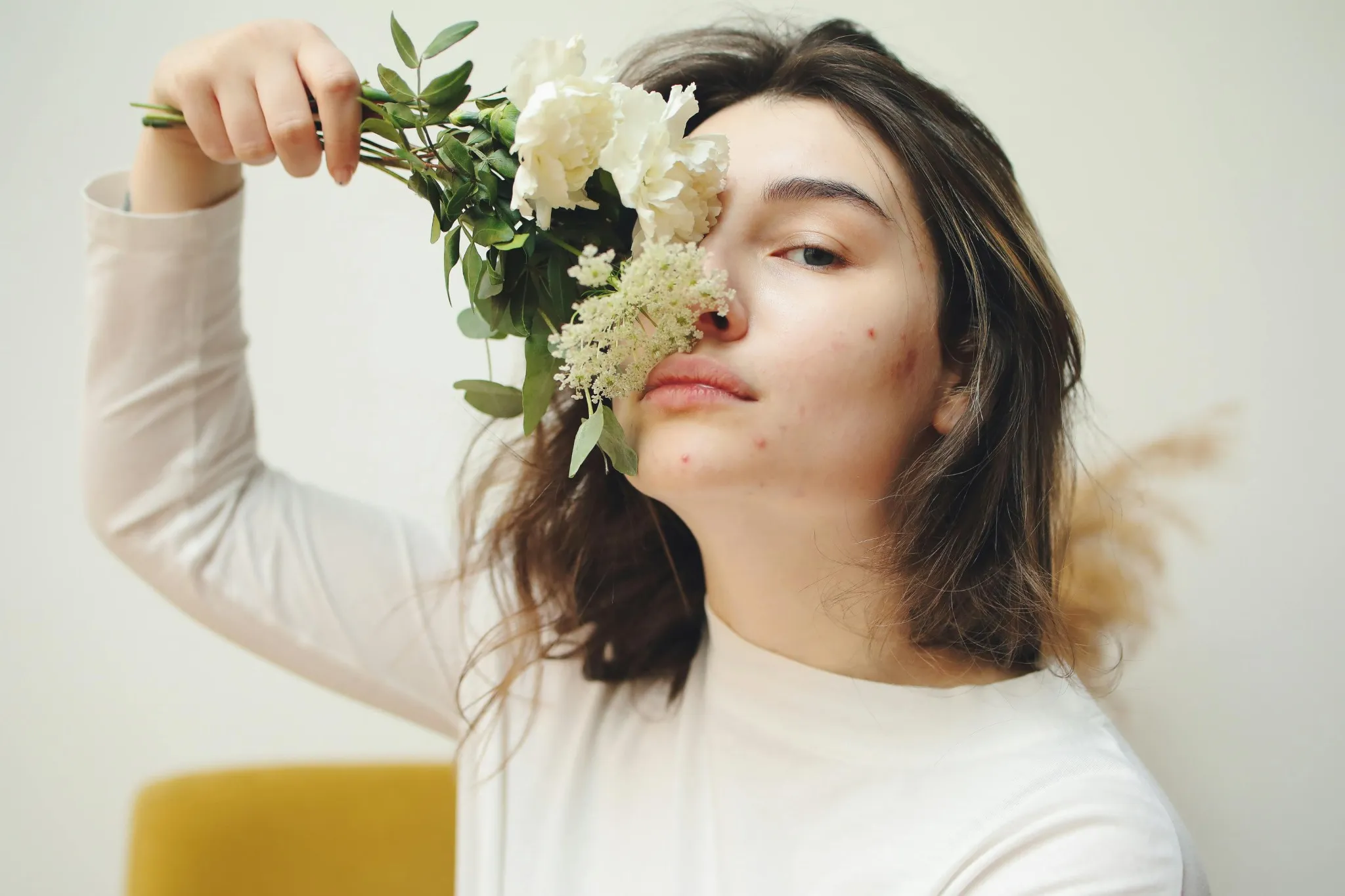 Girl covering half her face with flowers, Erase Acne scars of the past with the help of dermatologists